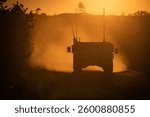 Silhouetted military vehicle driving on a dusty road at sunset, surrounded by trees and a distant watchtower.