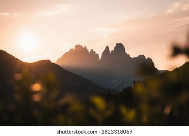 Silhouetted mountain range in an alpine setting during golden hour with haze in orange, pink, blue tones, a scenic wide landscape showcasing the natural scenery and outdoor environment.