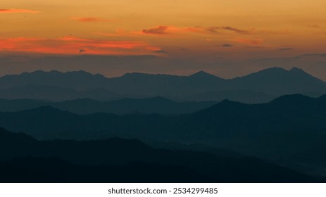 Silhouetted mountains overlap under a gradient sky, transitioning from warm amber to deep blue, with soft clouds scattered throughout. - Powered by Shutterstock