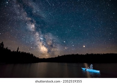 A silhouetted person in a kayak, illuminated by a brilliant night sky filled with stars
