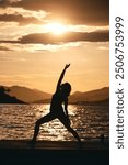 Silhouetted person performing a yoga pose by a tranquil lakeside during sunset, with scenic mountains and tranquil water in the background enhancing the serene atmosphere.