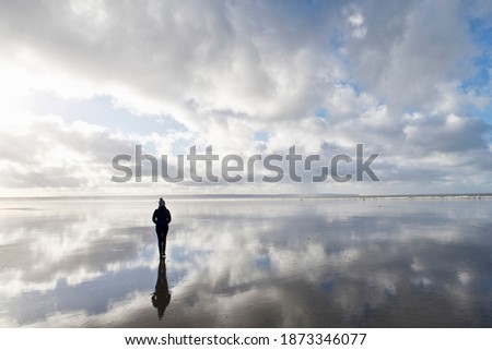 Silhouetted reflection of a woman standing on the wet portion of the beach during low tide