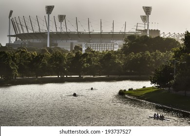 Silhouetted rowers on the Yarra River with the Melbourne Cricket Ground in the background.