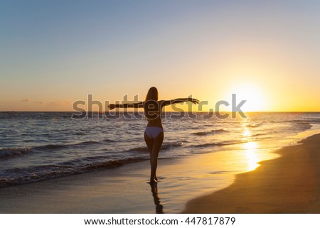 Silhouetted young woman with arms open on beach at sunset, Dominican Republic, The Caribbean