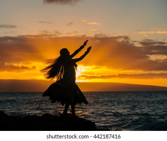 Silhouetted young woman in traditional costume, hula dancing on coastal rock at sunset, Maui, Hawaii, USA - Powered by Shutterstock