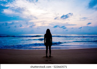 Silhouettes of an alone woman looking at view on the beach with sea and sunset background