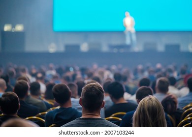 Silhouettes Of Anonymous People Sitting In Dark Auditorium And Listening To Speaker Talking From Stage During Business Seminar