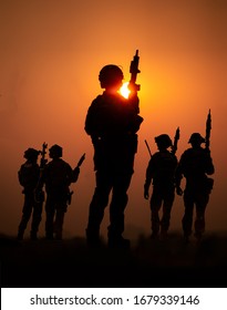 Silhouettes of army soldiers against the sun, U.S. marines team in action, surrounded fire and smoke, shooting with assault rifle and machine gun, attacking enemy
