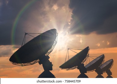 Silhouettes Of Array Of Satellite Dishes Or Radio Antennas At Sunset.