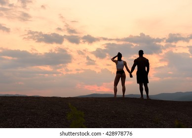 Silhouettes of athletic gymnastic couple watching the sunrise together. Beauty and perfection of human's body