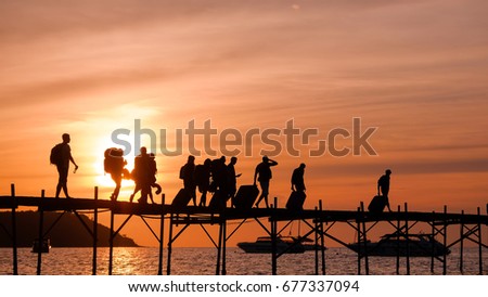 Silhouettes of the backpackers walking along the wooden pier to the ferry on beautiful sunset time. Tourists with bags walk along the Bang Rack pier to the ferry to Phangan island