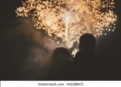 Silhouettes of bride and groom watching fireworks in night sky