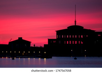 Silhouettes of buildings on the seashore against red sunset. The sunset glaring through the windows