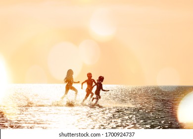 Silhouettes of children running through the water in the sea at sunset, backlit