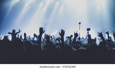 silhouettes of concert crowd in front of bright stage lights. Dark background, smoke, concert  spotlights - Shutterstock ID 576741349
