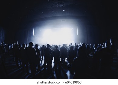 Silhouettes Of Concert Crowd In Front Of Bright Stage Lights. Dark Background, Smoke, Concert  Spotlights. Empty Hall