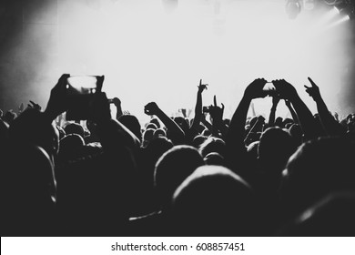 silhouettes of concert crowd in front of bright stage lights. Dark background, smoke, concert  spotlights. Group of people holding hands with mobile phones at a concert 