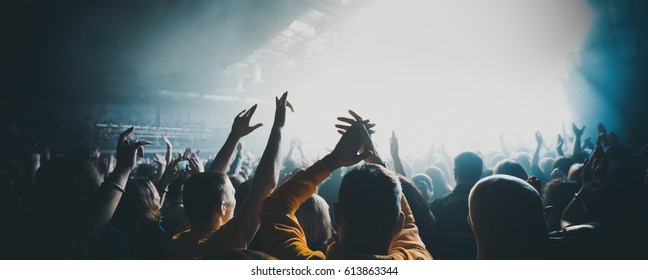 silhouettes of concert crowd in front of bright stage lights. Dark background, smoke, concert  spotlights - Shutterstock ID 613863344