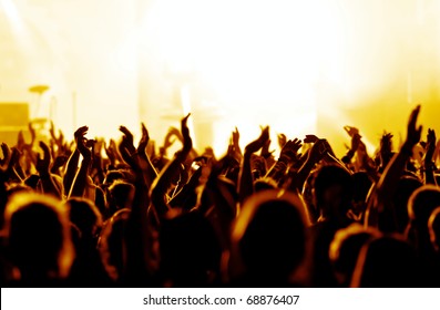 silhouettes of concert crowd in front of bright yellow/white stage lights