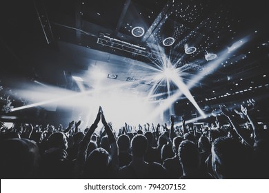 silhouettes of concert crowd in front of bright stage lights. Dark background, smoke, concert  spotlights, disco ball