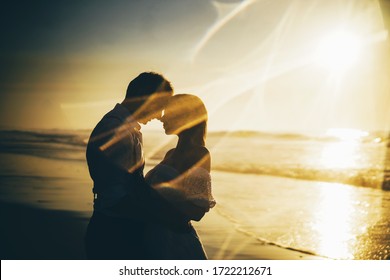 Silhouettes couple staying on the beach with sunset on background.