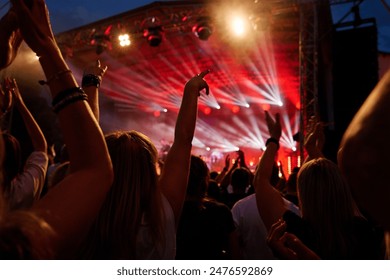 Silhouettes of crowd at concert in front of stage with bright spotlights. People enjoy live music at the band's performance. Concert hall with musicians on stage and fans during music festival