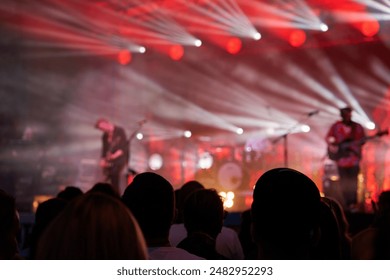 Silhouettes of crowd at concert in front of stage with bright spotlights. People enjoy live music at the band's performance. Concert hall with musicians on stage and fans during music festival - Powered by Shutterstock