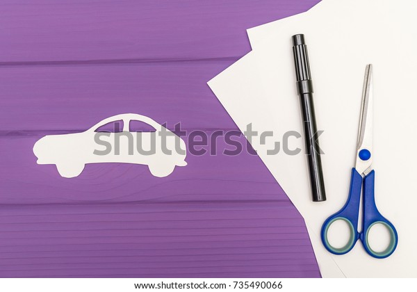 The silhouettes cut out of paper of car, scissors\
and marker near on a white sheet of paper on purple wooden\
background, car insurance\
concept