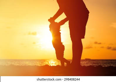 silhouettes of father and little daughter walking on beach at sunset