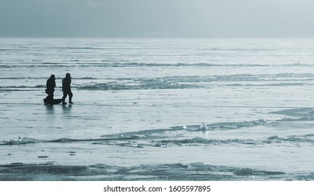 Silhouettes Of Fishermen On An Ice Floe On A Winter Day. Dangerous Fishing On Thin Ice Concept