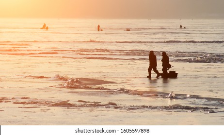 Silhouettes Of Fishermen On An Ice Floe On A Winter Day. Dangerous Fishing On Thin Ice Concept