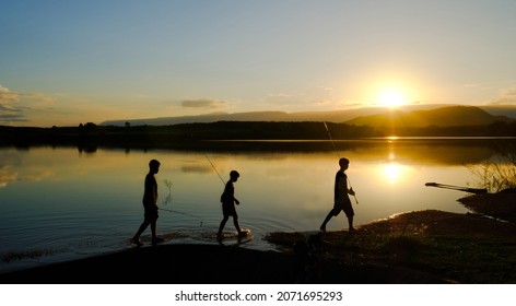 Silhouettes of fishing boys are walking home after fishing the lake in the evening sun, Reservoir Amphoe Wang Saphung Loei Thailand - Powered by Shutterstock