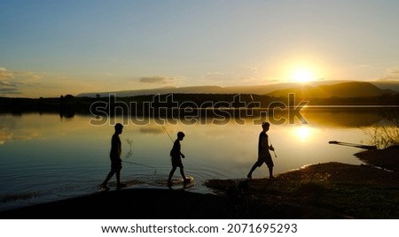 Silhouettes of fishing boys are walking home after fishing the lake in the evening sun, Reservoir Amphoe Wang Saphung Loei Thailand