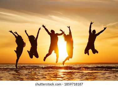 Silhouettes Of Five Happy Jumping Friends In Water At Sunset Time