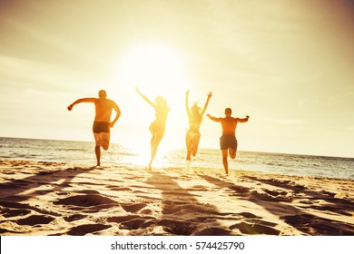 Silhouettes of four friends runs at sunset beach to the sea - Powered by Shutterstock