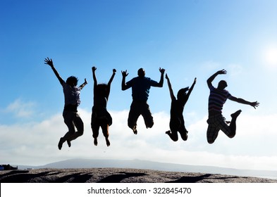Silhouettes of group of friends jumping outdoors on a beach in unison with arms up