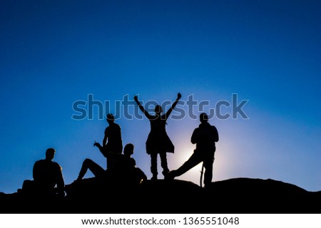 Silhouettes of a group of people on top of a cliff with the sun behind them. Hikers on top of a cliff.