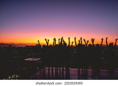 Silhouettes of a group of persons celebrating in the rooftop with a panoramic view of the city and skyline with colorful sunset sky, Santiago, Chile - Powered by Shutterstock