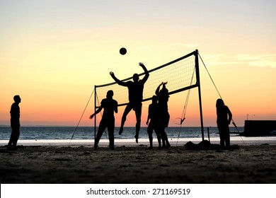 Silhouettes of a group of young people playing beach volleyball on the beach during sunset in Brittany, France