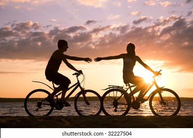 Silhouettes of happy couple stretching arms to each other while riding bicycles on seashore at sunset - Powered by Shutterstock