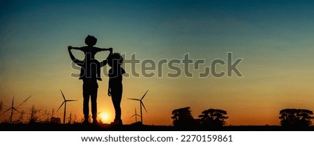 Silhouettes of Happy family father, mother and child daughter sits on the shoulders of his father with windmills for electricity generation at sunrise.