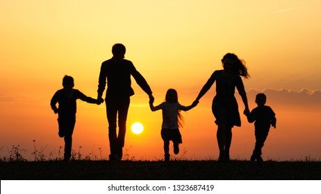 Silhouettes of happy family holding the hands in the meadow during sunset.