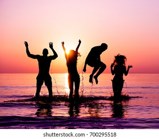 Silhouettes of happy friends jumping inside water on the beach at sunset - Group of young people having fun on summer vacation - Youth and friendship concept - Focus on bodies silhouette