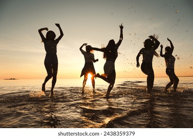 Silhouettes of happy girls are having fun and dancing at sunset lake beach - Powered by Shutterstock