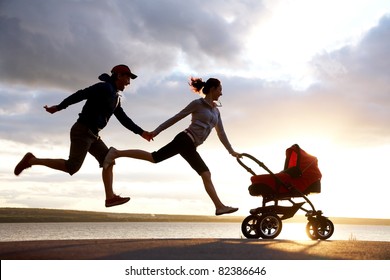 Silhouettes Of Happy Parents Are Running For A Pram