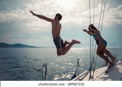 Silhouettes Of Happy People Jumping Into Water From A Boat - Friends Diving And Having Fun On A Summer Vacation