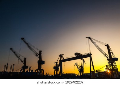 Silhouettes of harbor cranes at sunset. Shipyard at sunset. - Powered by Shutterstock