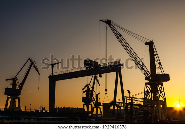 Silhouettes of harbor cranes at sunset. Shipyard\
at sunset.