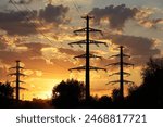 Silhouettes of high voltage towers with electrical wires on background of sunset sky and dark clouds. Electricity transmission lines in city, power supply concept