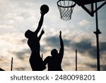 Silhouettes of an intense moment as a basketball player shoots the ball against a defending opponent